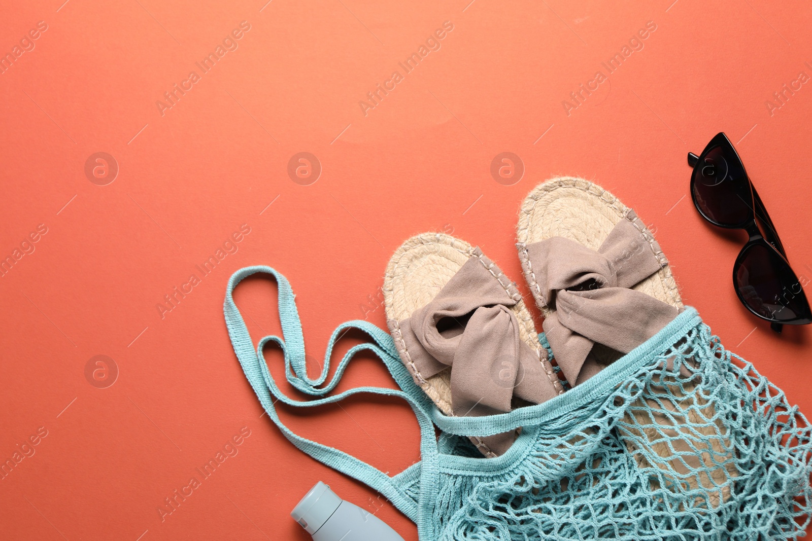 Photo of String bag, sunglasses, slippers and cosmetic product on coral background, top view. Space for text