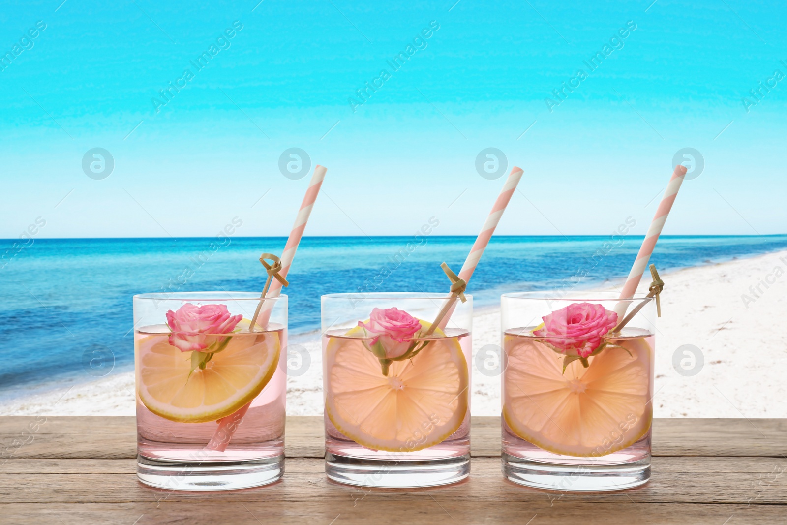 Image of Tasty refreshing drink on wooden table against sandy beach