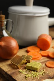Photo of Bouillon cubes, onion and cut carrot on wooden board