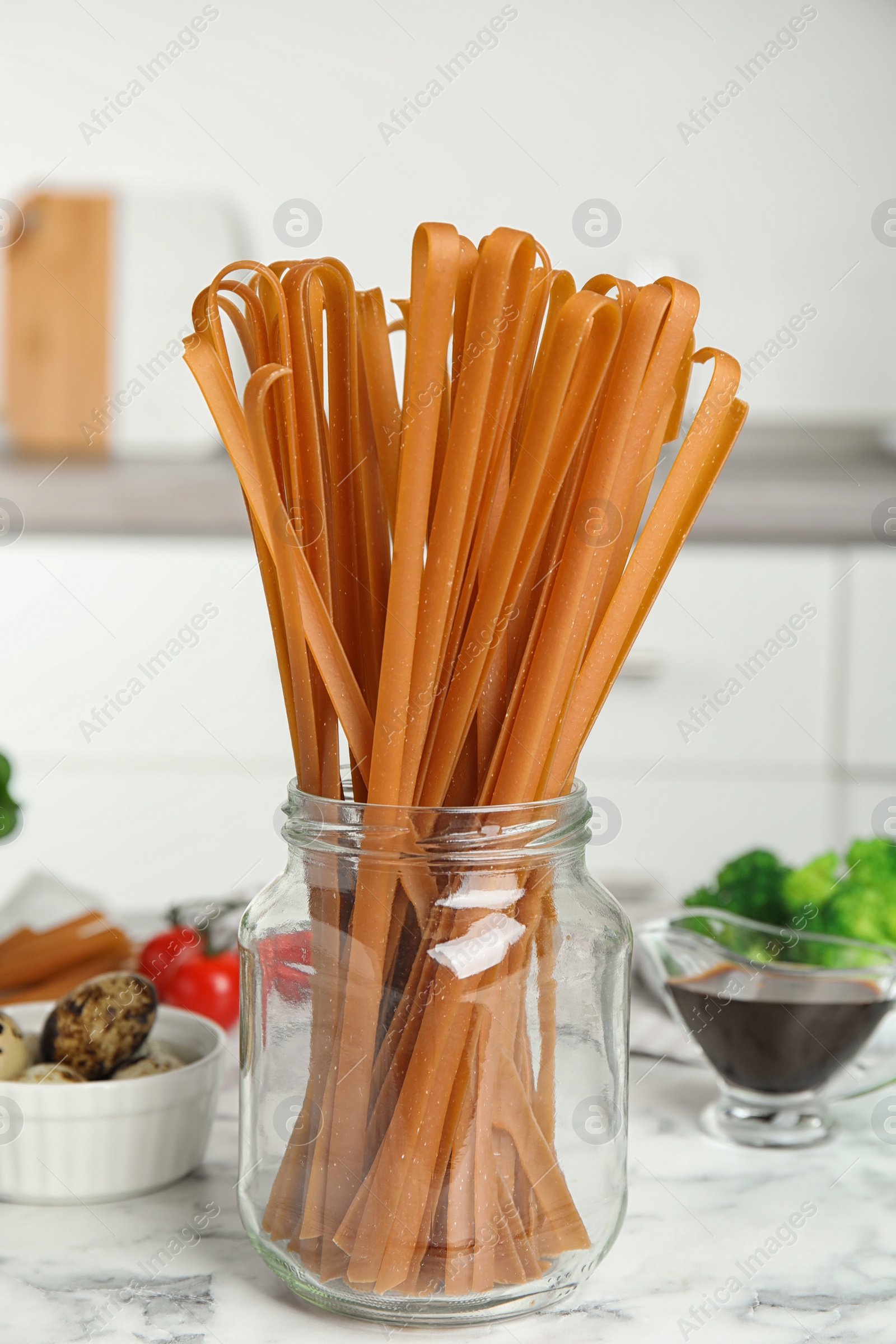 Photo of Uncooked buckwheat noodles and fresh ingredients  on white marble table in kitchen