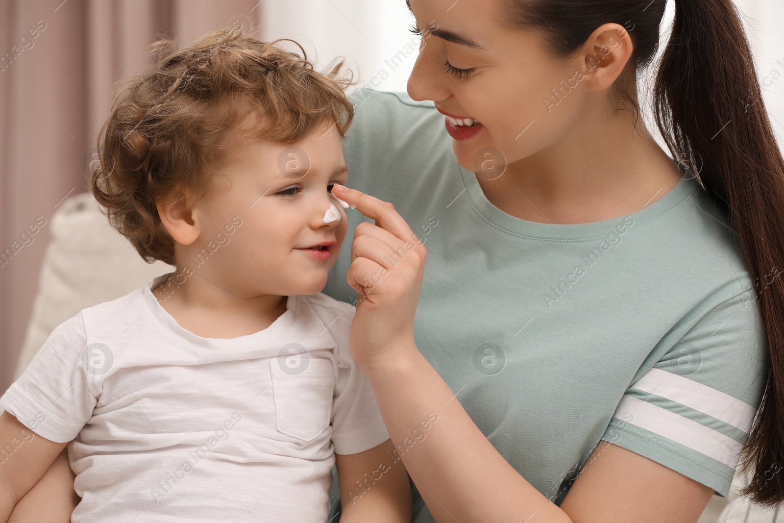 Photo of Mother applying ointment onto her son`s nose indoors