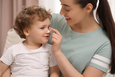Photo of Mother applying ointment onto her son`s nose indoors
