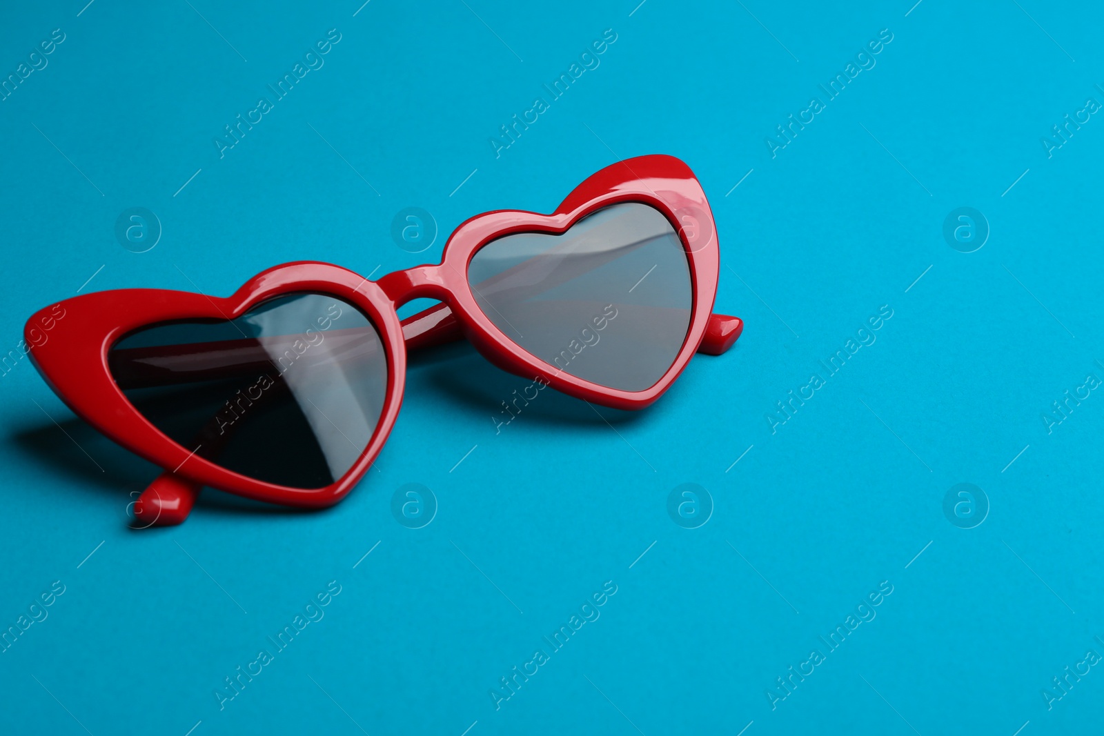 Photo of Stylish heart shaped sunglasses on blue background. Fashionable accessory