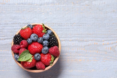 Different fresh ripe berries in bowl on light grey wooden table, top view. Space for text