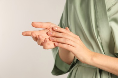Photo of Woman applying cosmetic cream onto hand on light grey background, closeup