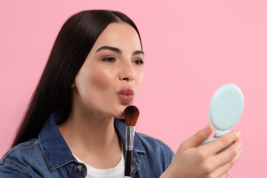 Photo of Beautiful woman with cosmetic pocket mirror and makeup brush on pink background