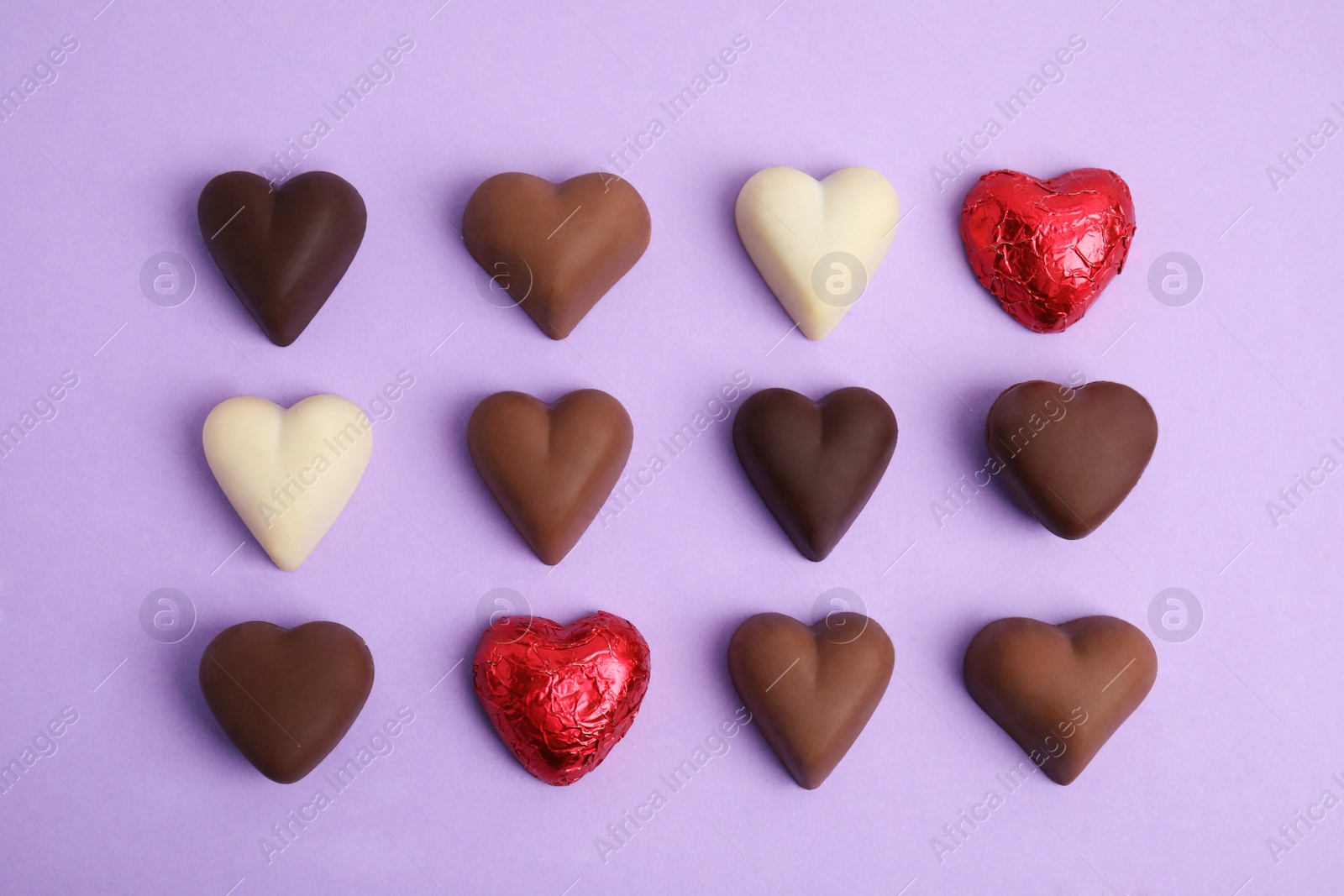 Photo of Tasty heart shaped chocolate candies on violet background, flat lay. Happy Valentine's day
