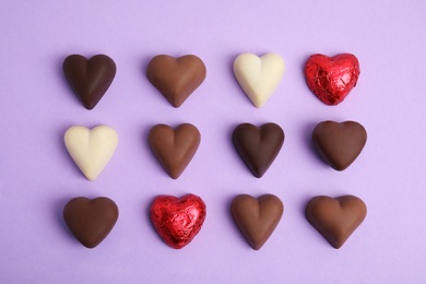 Photo of Tasty heart shaped chocolate candies on violet background, flat lay. Happy Valentine's day