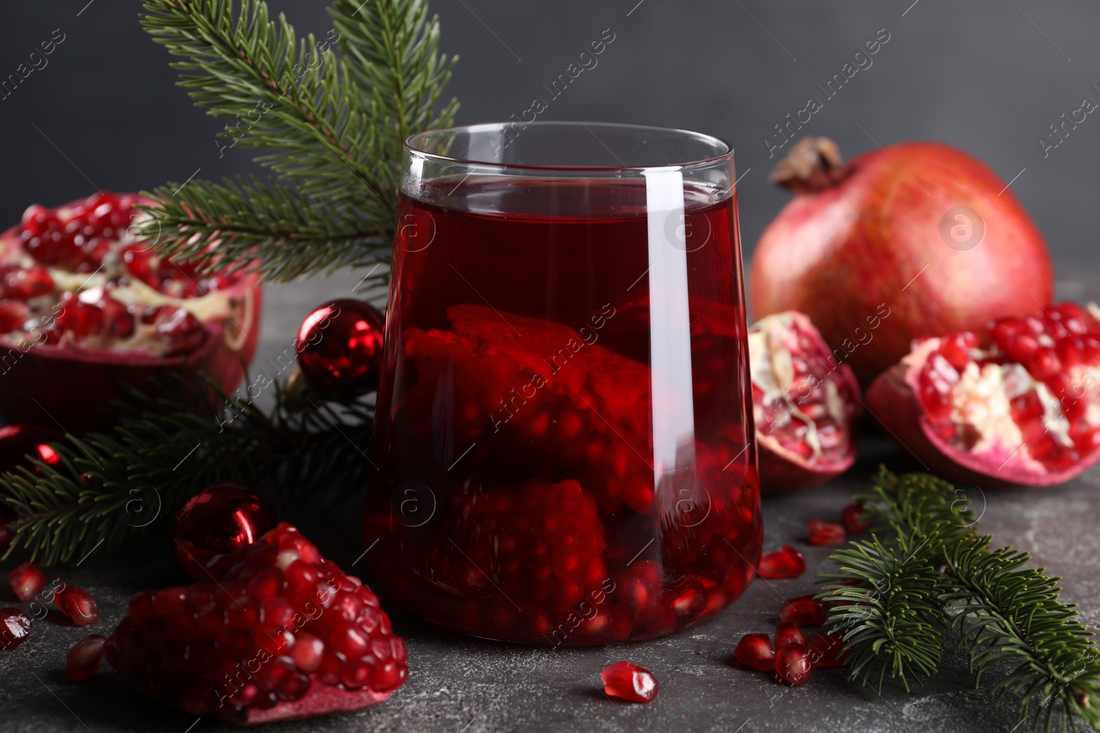 Photo of Aromatic Sangria drink in glass, Christmas decor and pomegranate grains on grey table