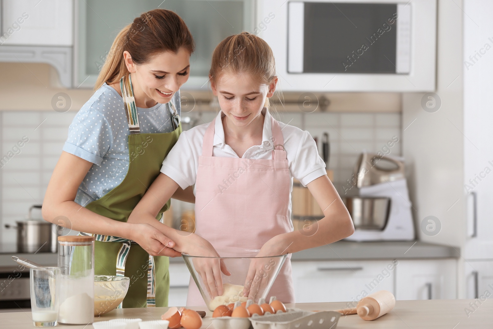 Photo of Mother and her daughter preparing dough at table in kitchen