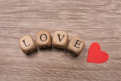 Photo of Mini cubes with letters forming word Love near red paper heart on wooden background, flat lay