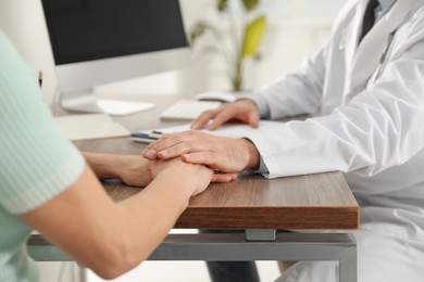 Photo of Doctor consulting patient at wooden table in clinic, closeup