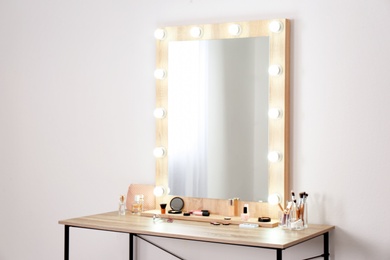Photo of Table with makeup products and mirror near white wall, space for text. Dressing room interior