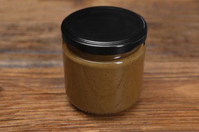 Photo of Tasty nut paste in jar on wooden table, closeup