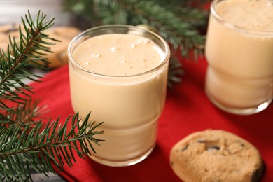 Photo of Tasty eggnog, cookies and fir branches on wooden table, closeup