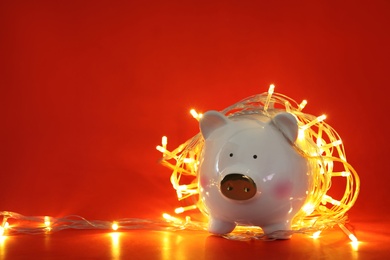 Photo of Piggy bank with Christmas lights on red background. Space for text