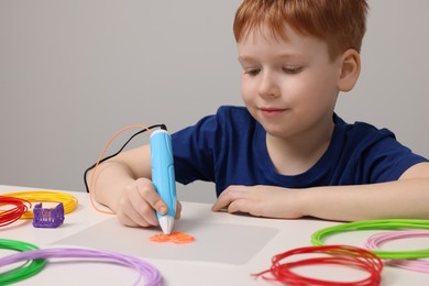 Boy drawing with stylish 3D pen at white table