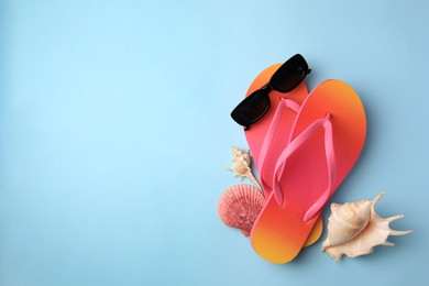 Photo of Sunglasses, flip flops and shells on light blue background, flat lay with space for text. Beach accessories