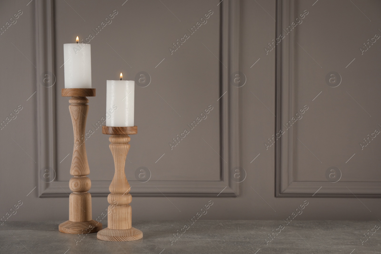 Photo of Elegant candlesticks with burning candles on grey table. Space for text