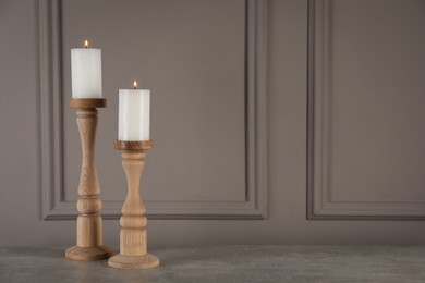 Elegant candlesticks with burning candles on grey table. Space for text