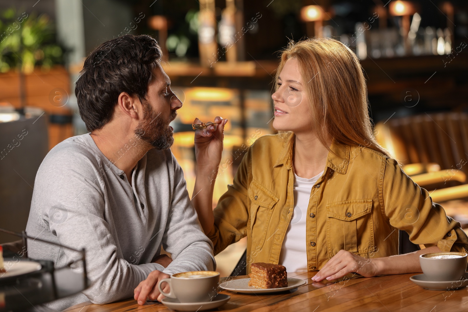 Photo of Romantic date. Beautiful woman feeding her boyfriend with cake in cafe