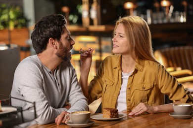 Photo of Romantic date. Beautiful woman feeding her boyfriend with cake in cafe