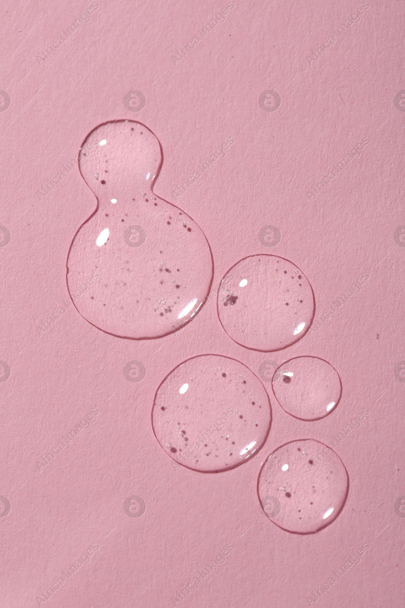 Photo of Drops of cosmetic serum on pink background, top view.