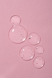 Drops of cosmetic serum on pink background, top view.