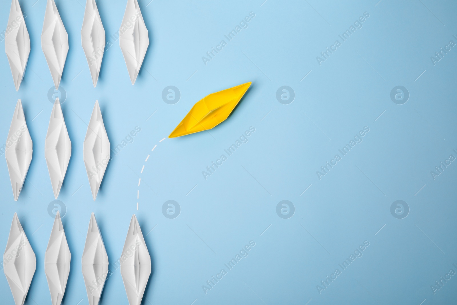 Photo of Yellow paper boat floating away from others on light blue background, flat lay with space for text. Uniqueness concept