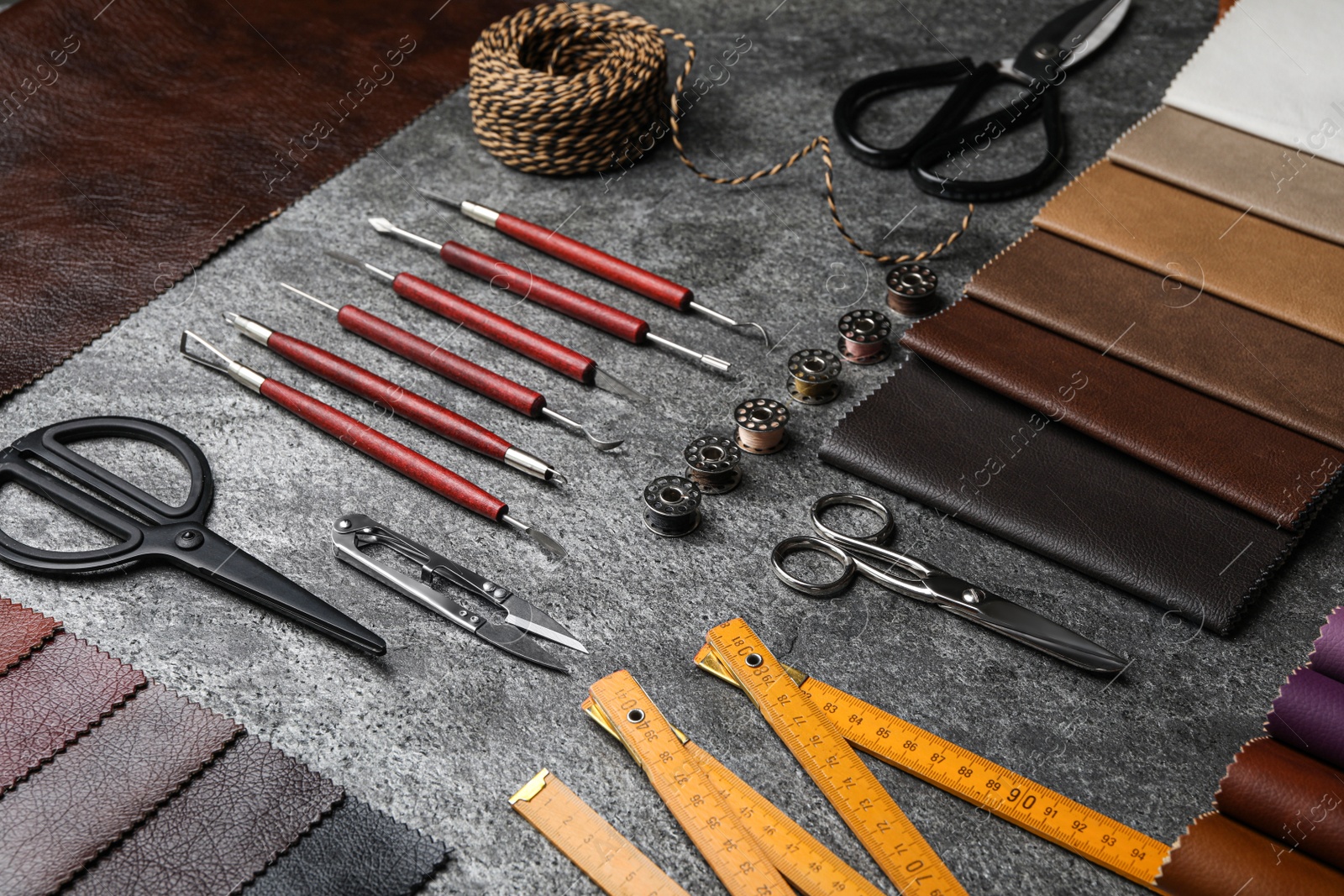 Photo of Leather samples and craftsman tools on grey stone background