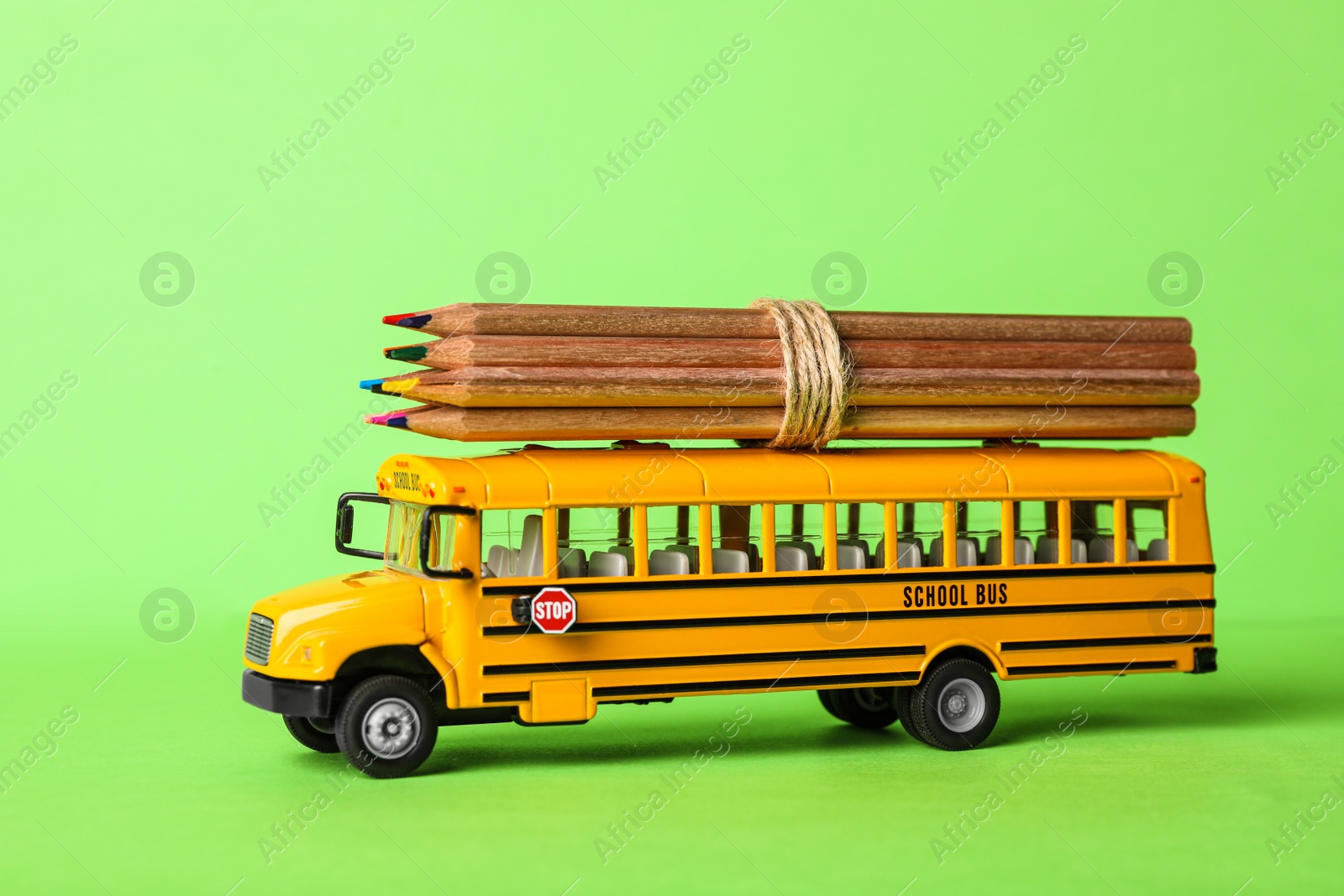 Photo of School bus model with color pencils on green background. Transport for students