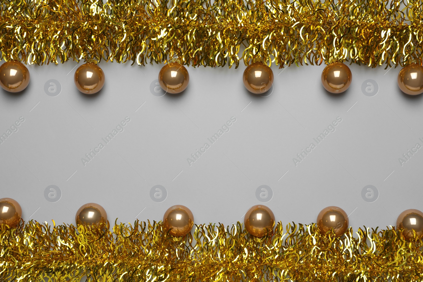 Photo of Golden tinsel and Christmas balls on light grey background, flat lay. Space for text