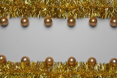 Golden tinsel and Christmas balls on light grey background, flat lay. Space for text