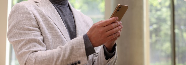 Image of Businessman typing message on mobile phone indoors, closeup. Banner design
