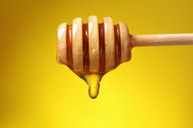 Delicious honey flowing down from dipper against yellow background, closeup