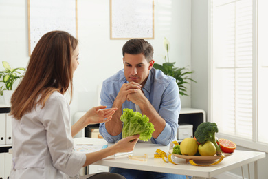 Young nutritionist consulting patient at table in clinic