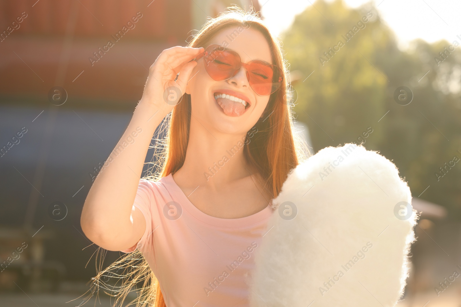 Photo of Funny woman with cotton candy showing tongue outdoors on sunny day