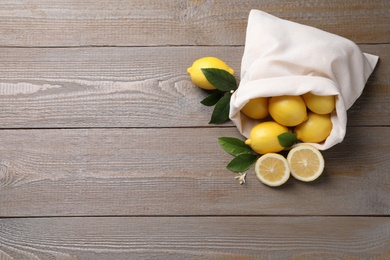 Many fresh ripe lemons with green leaves on wooden table, flat lay. Space for text