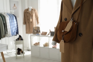 Photo of Stylish woman's clothes, shoes, accessories in modern boutique, focus on mannequin with coat and bag