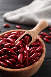 Photo of Raw red kidney beans in bowl and scoop on dark wooden table, closeup