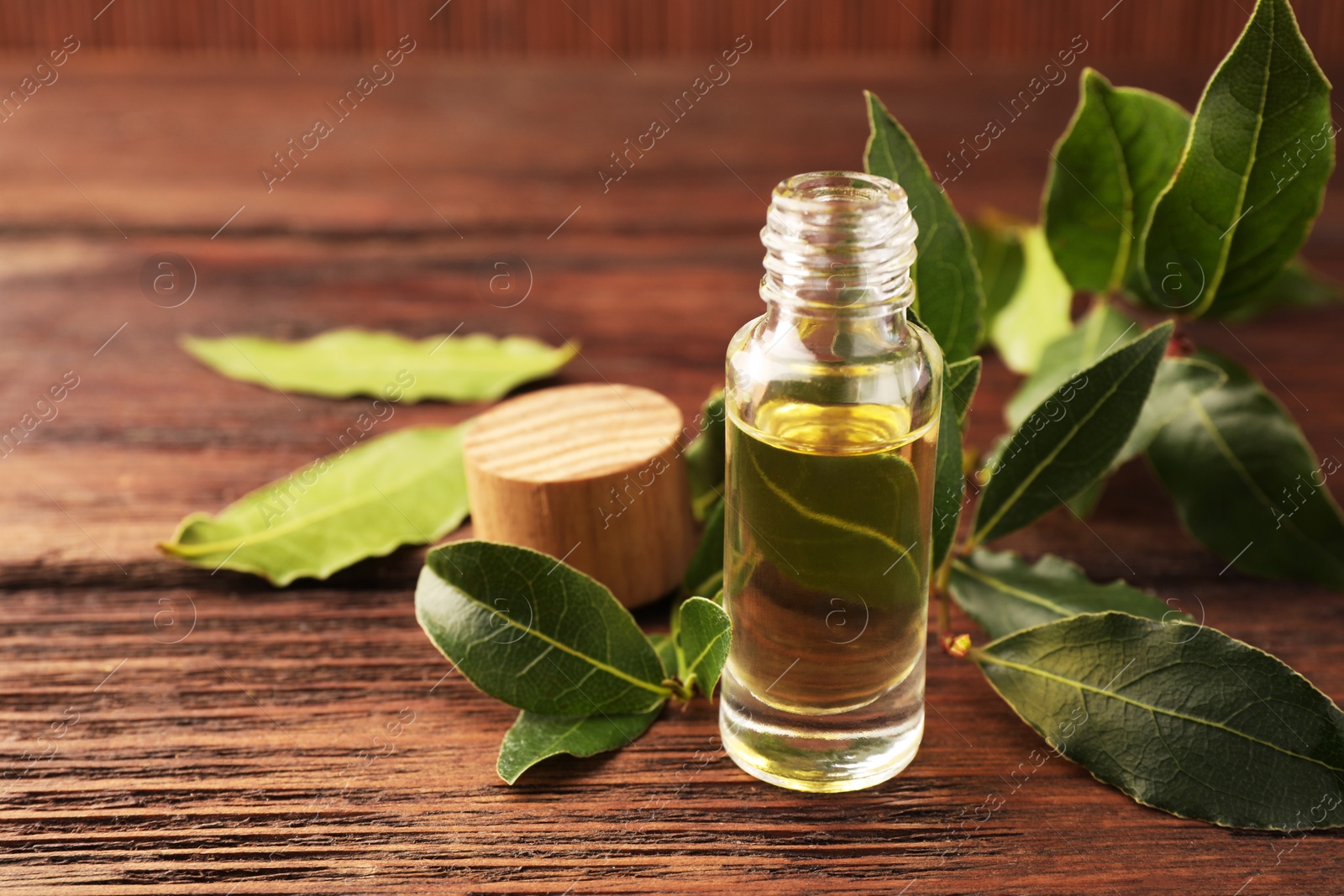 Photo of Bottle of bay essential oil and fresh leaves on wooden table. Space for text