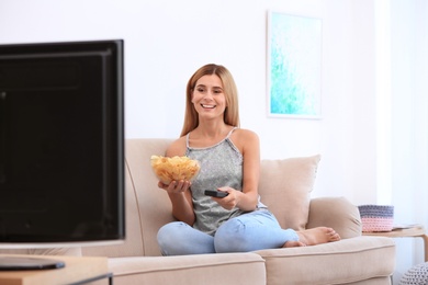 Photo of Woman with bowl of potato chips watching TV on sofa in living room