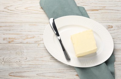 Photo of Block of tasty butter and knife on white wooden table. Space for text