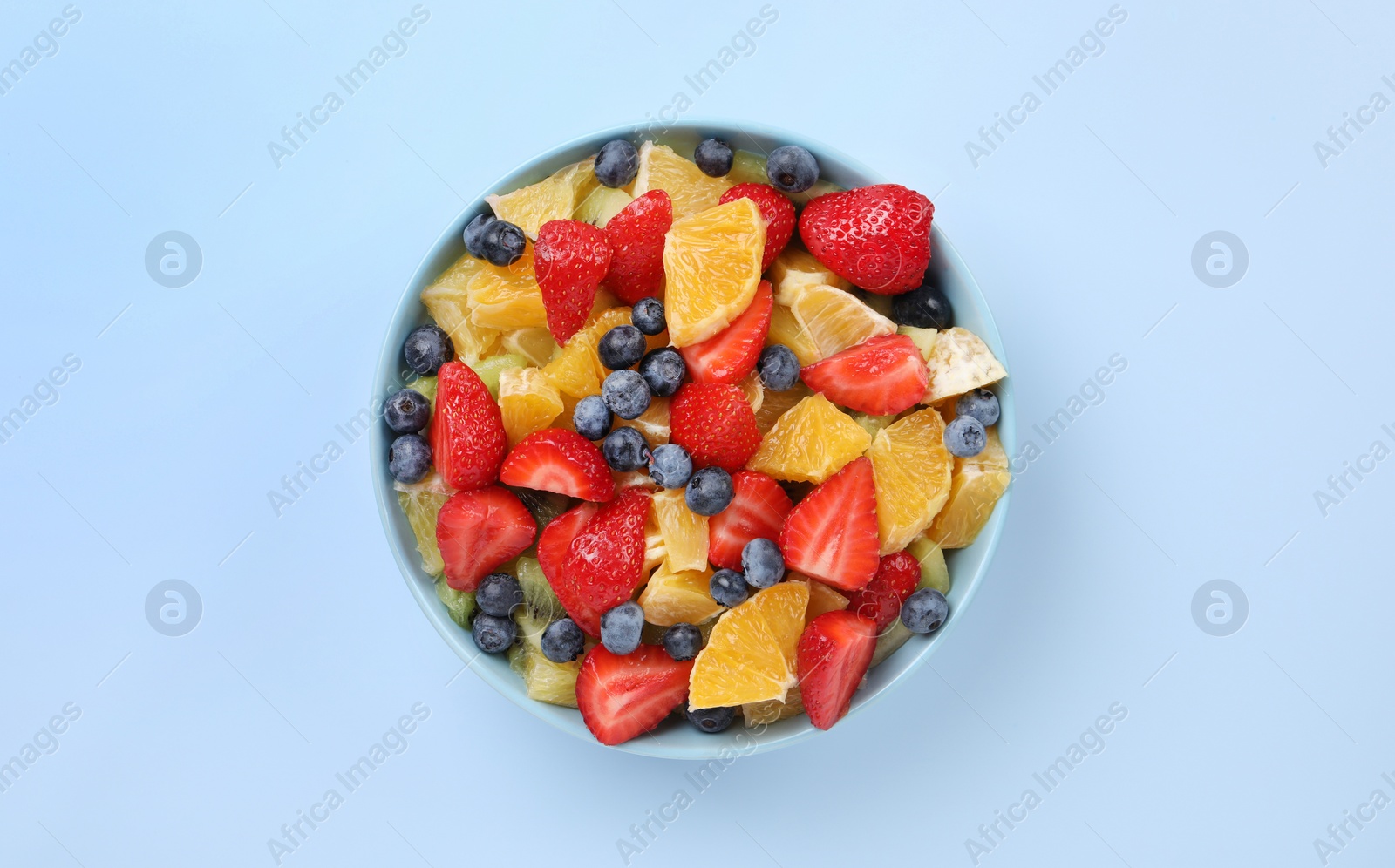 Photo of Yummy fruit salad in bowl on light blue background, top view