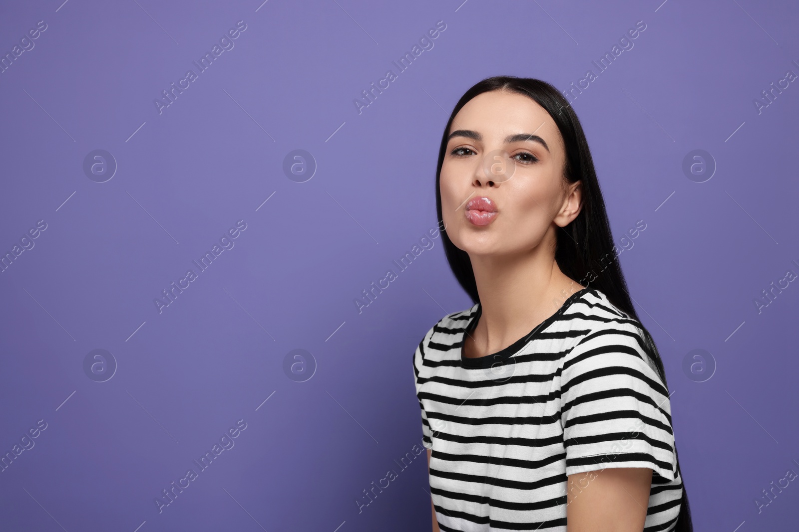 Photo of Beautiful young woman blowing kiss on purple background. Space for text