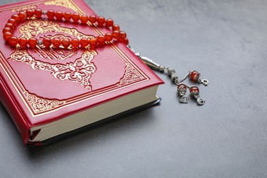 Photo of Muslim prayer beads and Quran on grey stone table, closeup. Space for text