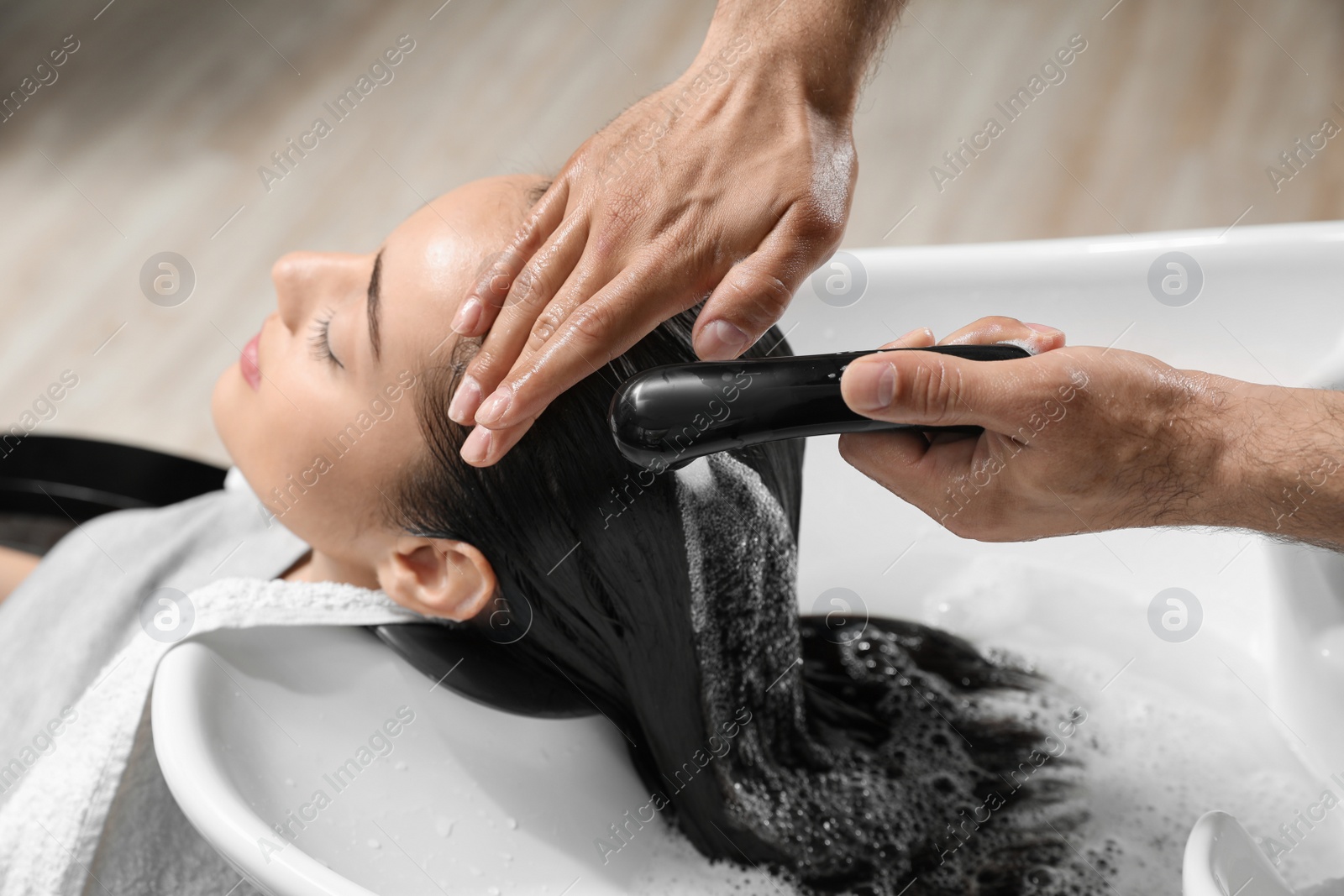 Photo of Stylist washing client's hair at sink in beauty salon