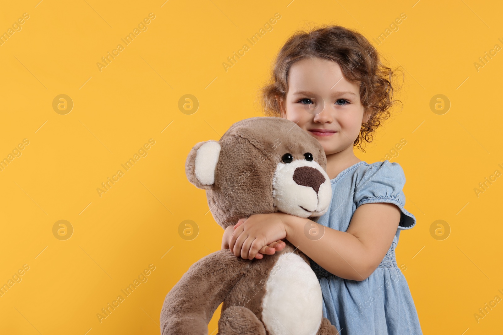 Photo of Cute little girl with teddy bear on orange background, space for text