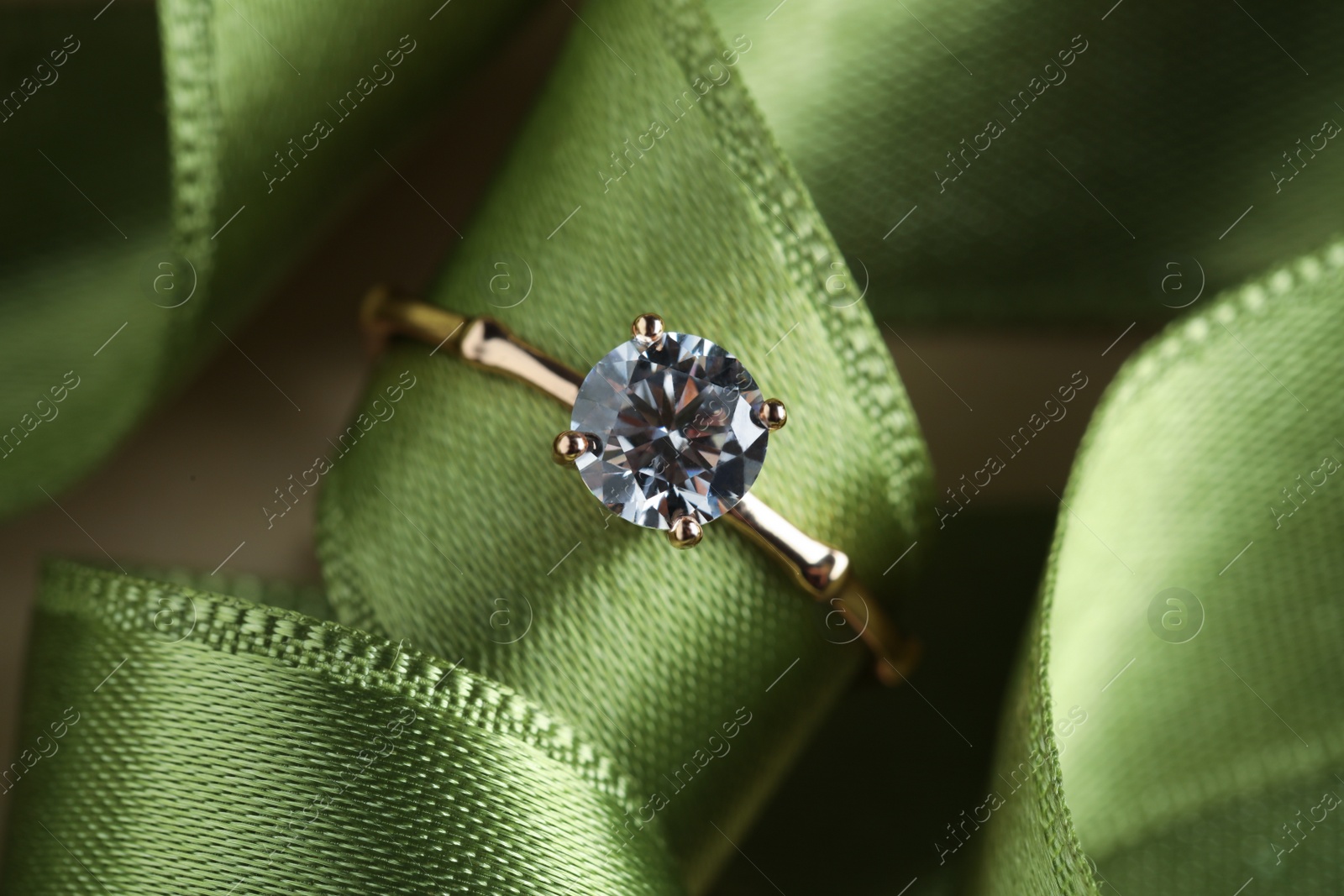 Photo of Beautiful engagement ring with gemstone on green ribbon, closeup