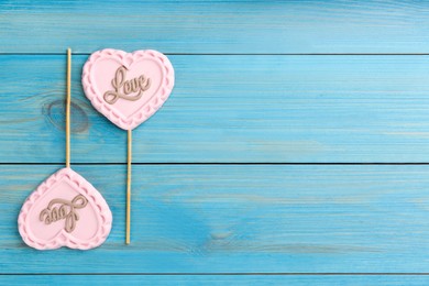 Photo of Chocolate heart shaped lollipops with word Love on turquoise wooden table, flat lay. Space for text